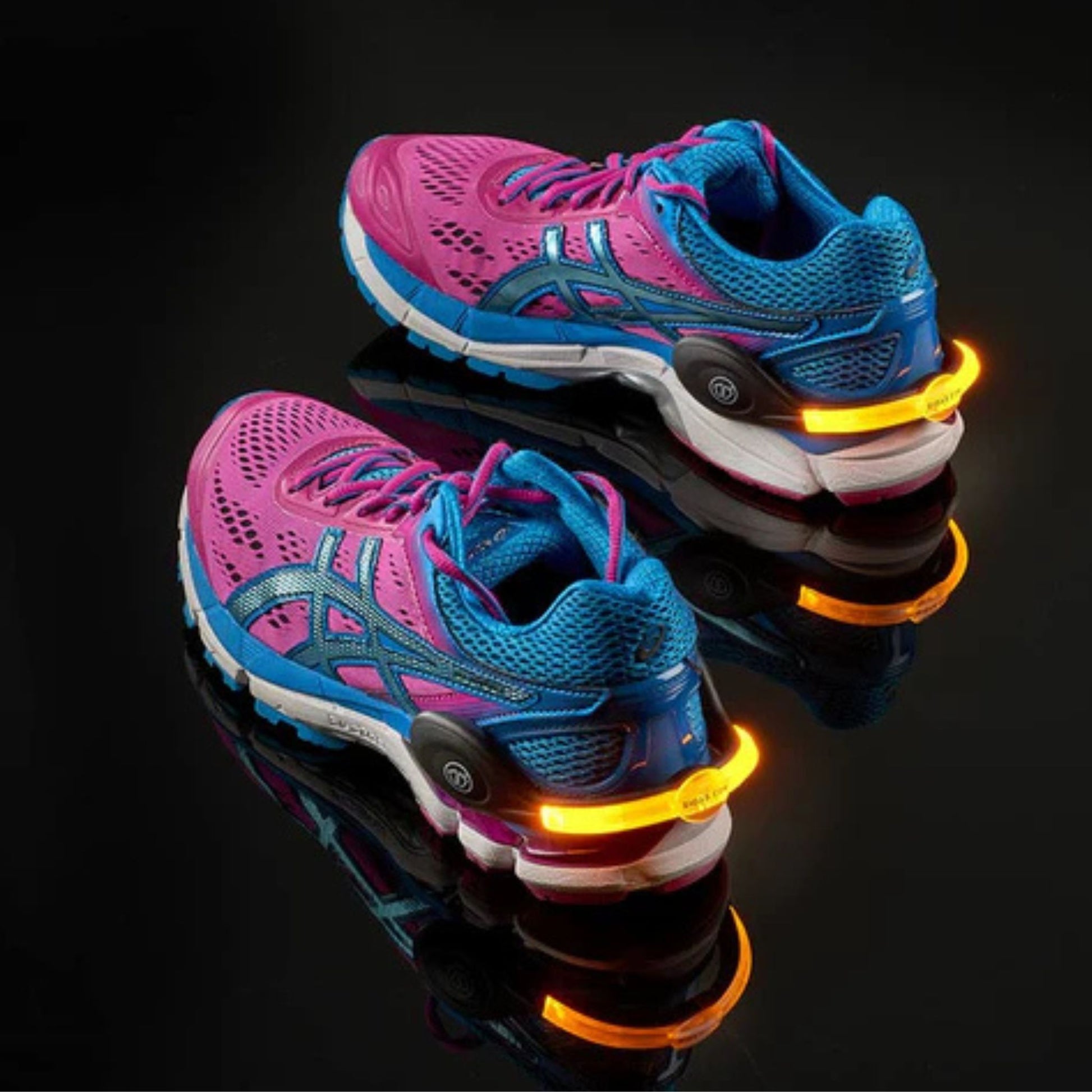 Pair of blue and pink running shoes with glowing orange lights on a reflective black surface.