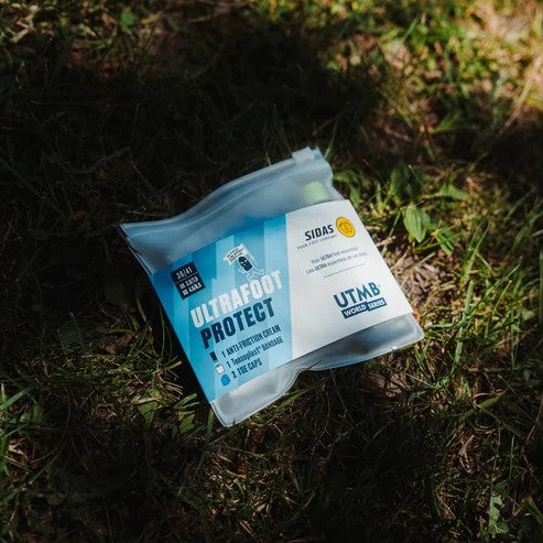 A clear plastic pouch of Sidas Ultrafoot Protect foot care cream lies on grass outdoors in dappled sunlight and shadow.